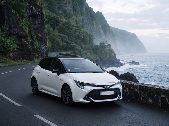 Toyota Corolla Hybride blanche garée sur une route côtière, au pied des falaises