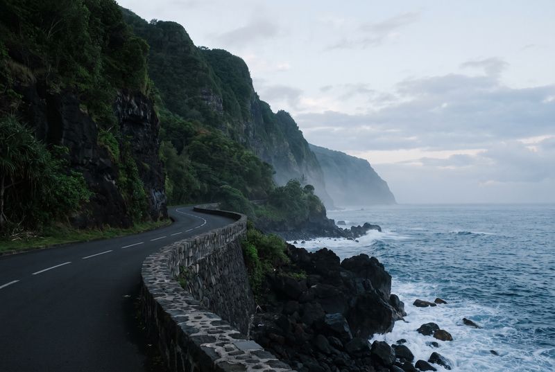 Route côtière au pied de falaises volcaniques couvertes de végétation, au bord de l’océan, à l’aube